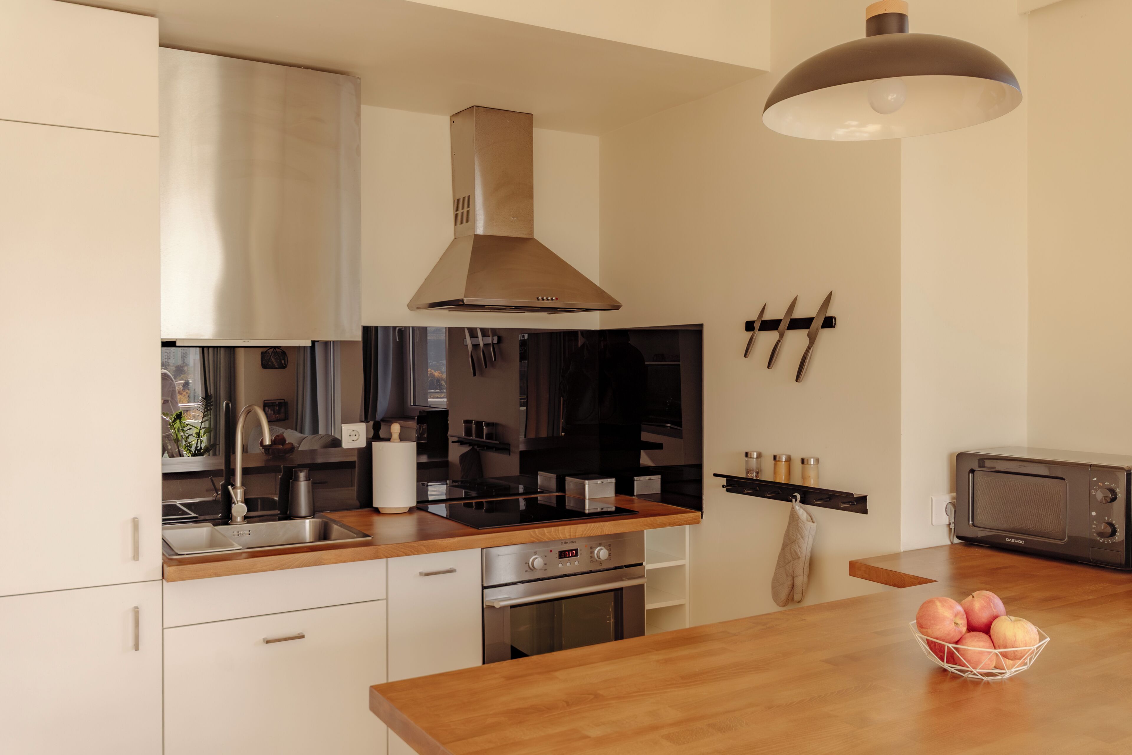 A modern kitchen with stainless steel appliances, a wooden countertop, and a hanging light fixture.