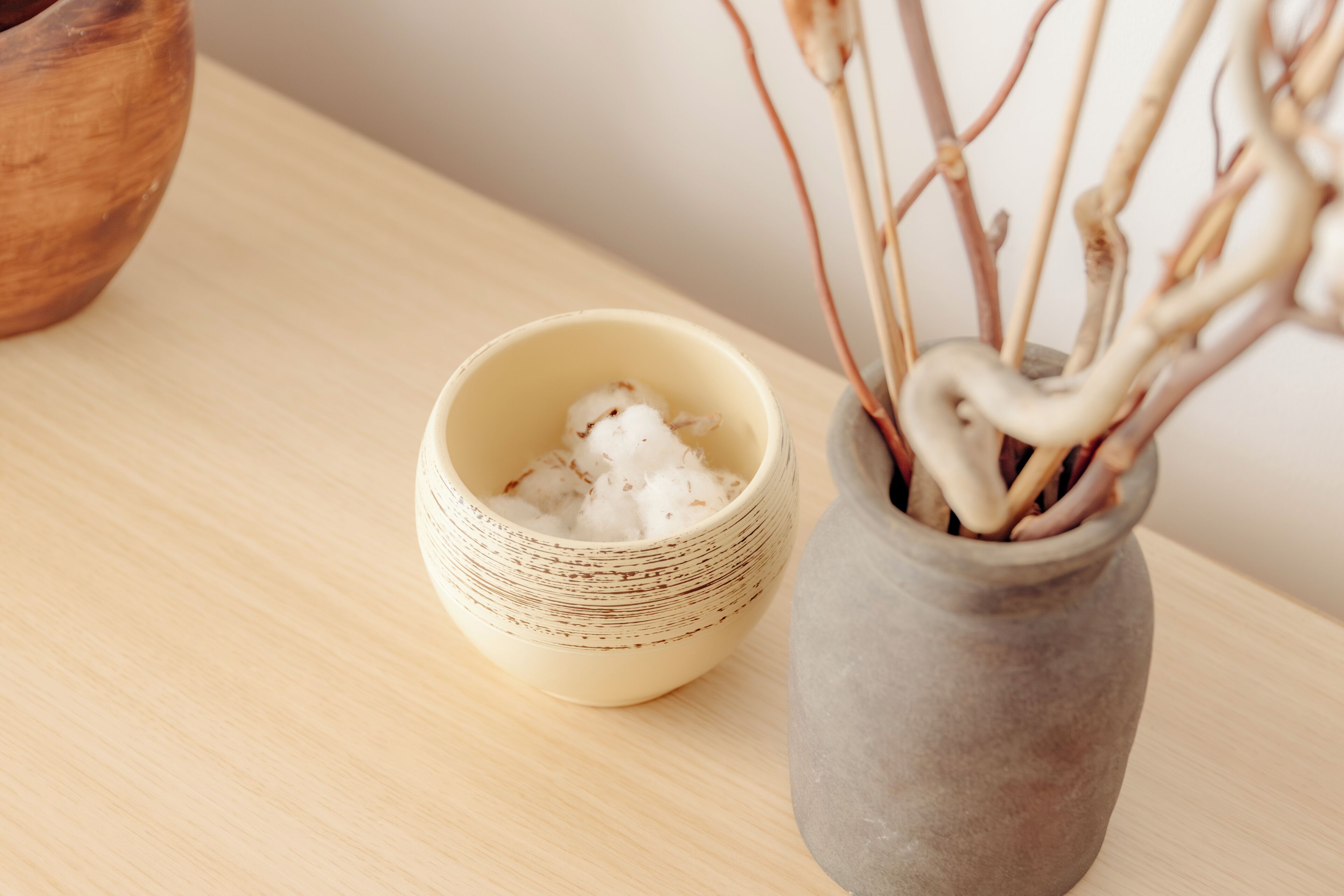 Una mesa de madera con un cuenco de cerámica que contiene material blanco y un florero con ramas.