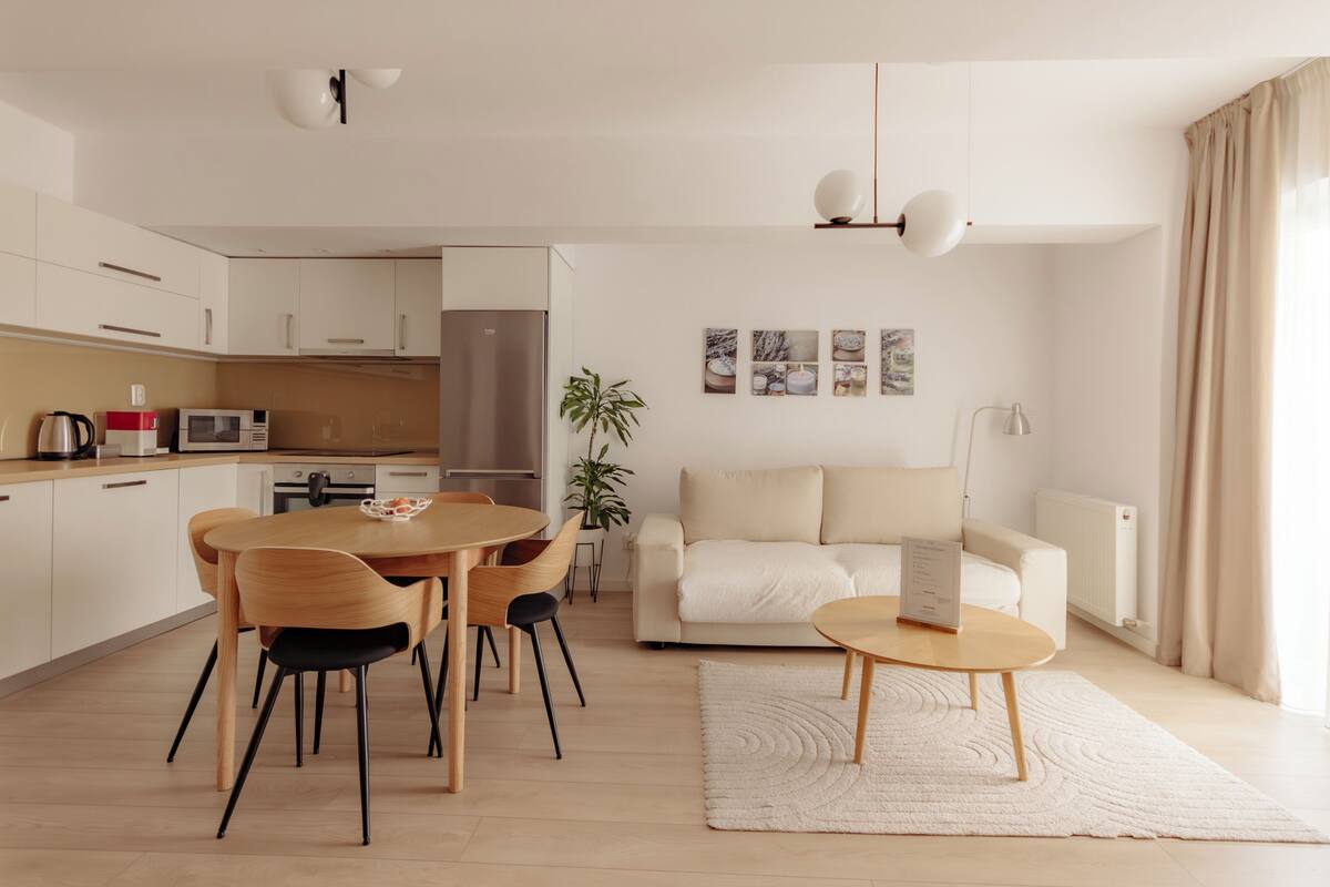Uma sala de estar moderna com área de jantar, um sofá, mesa de centro e cozinha ao fundo.