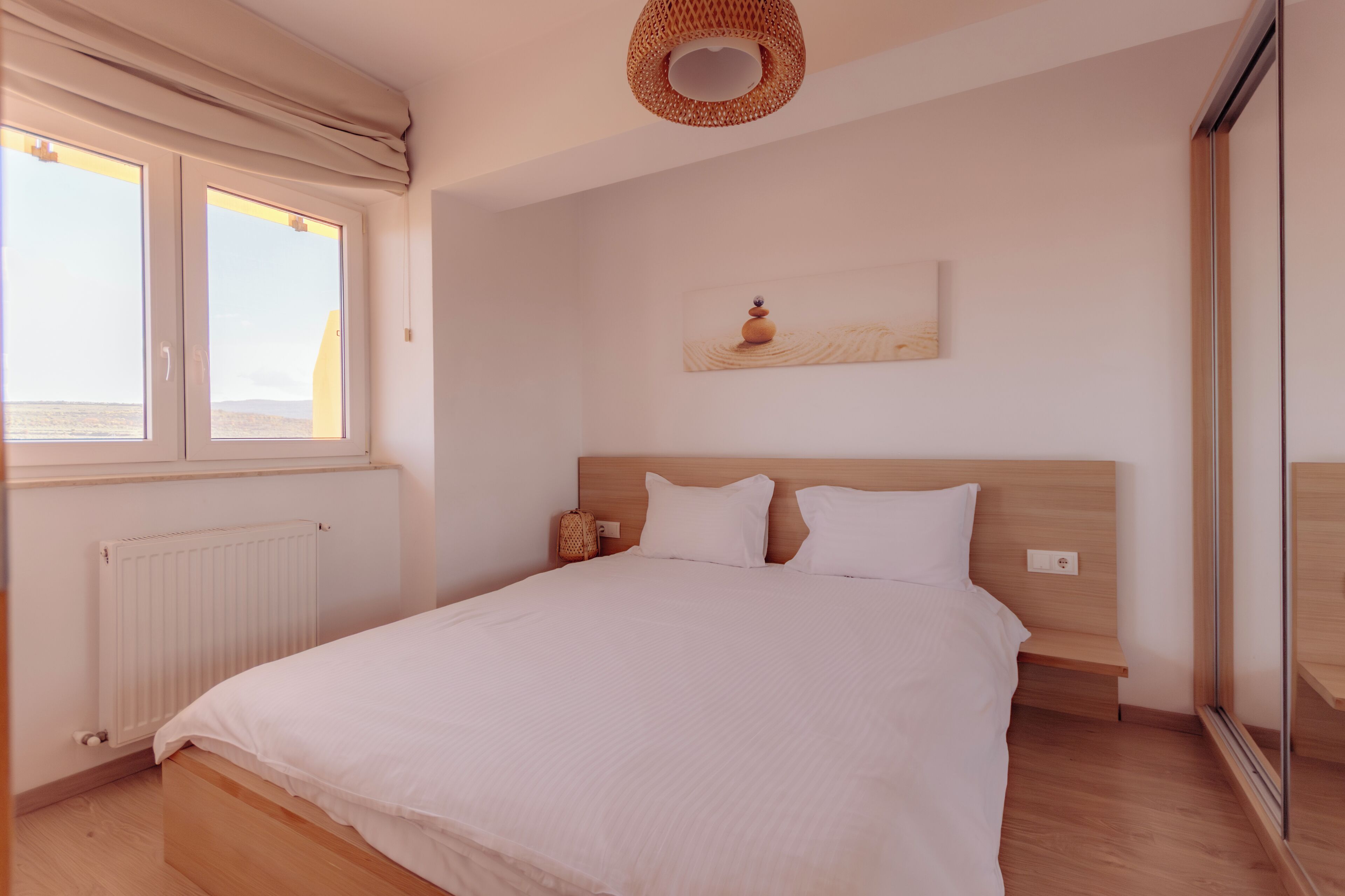 Une chambre à coucher comprenant un lit, une fenêtre, un radiateur, une table de chevet et une œuvre d’art accrochée au mur.