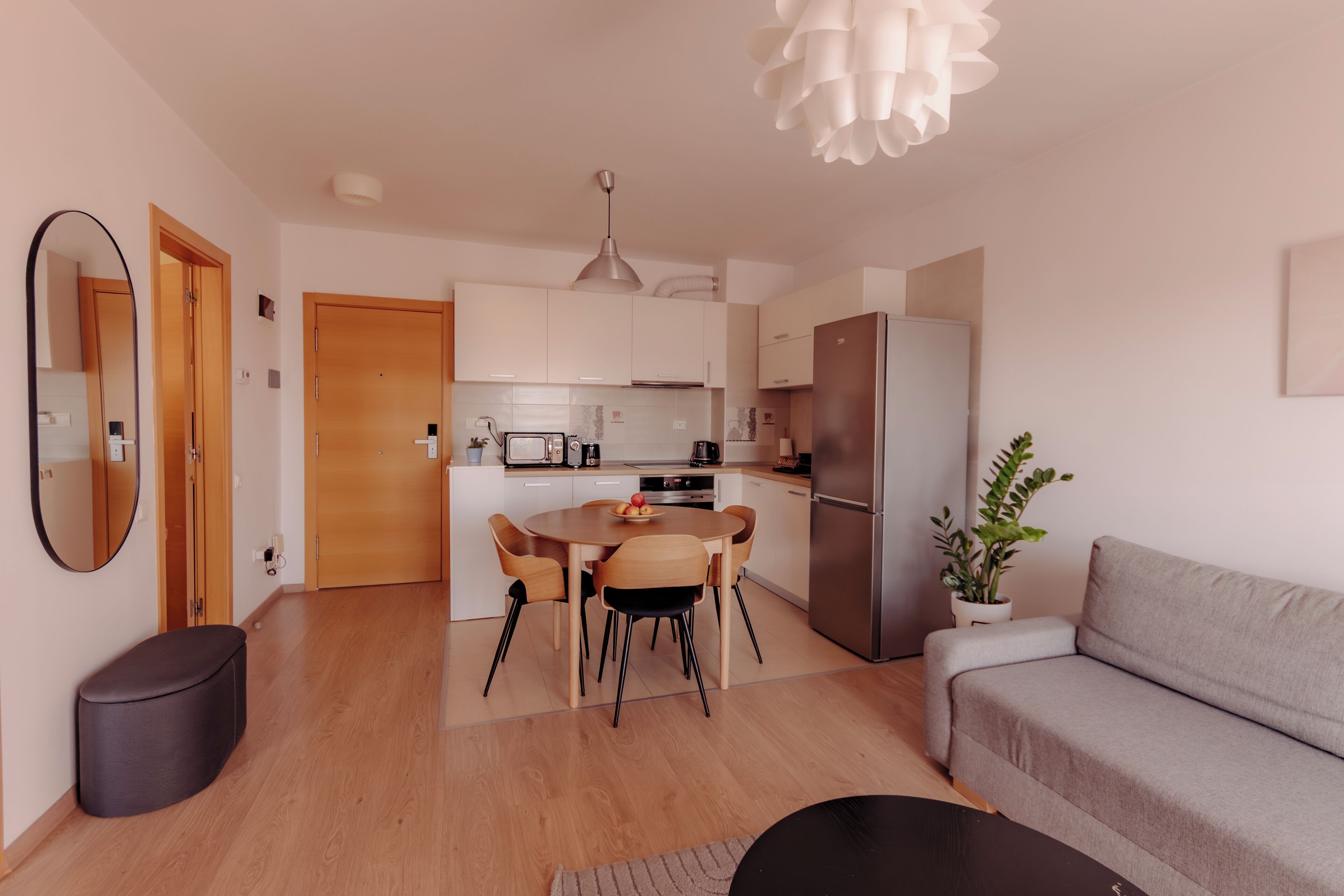 A modern kitchen with wooden cabinets, a dining table with chairs, a sofa, and a potted plant.