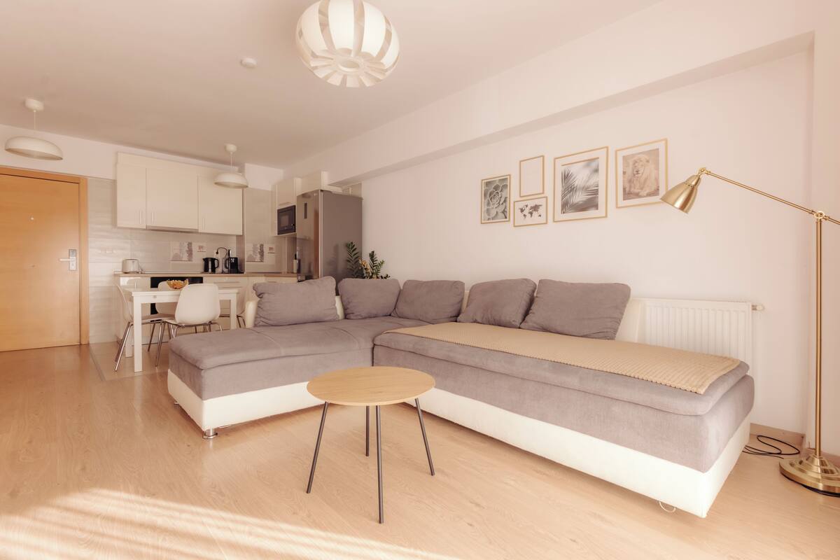 Uma sala de estar moderna com sofá modular, mesa de centro redonda e área de jantar com mesa e cadeiras brancas.