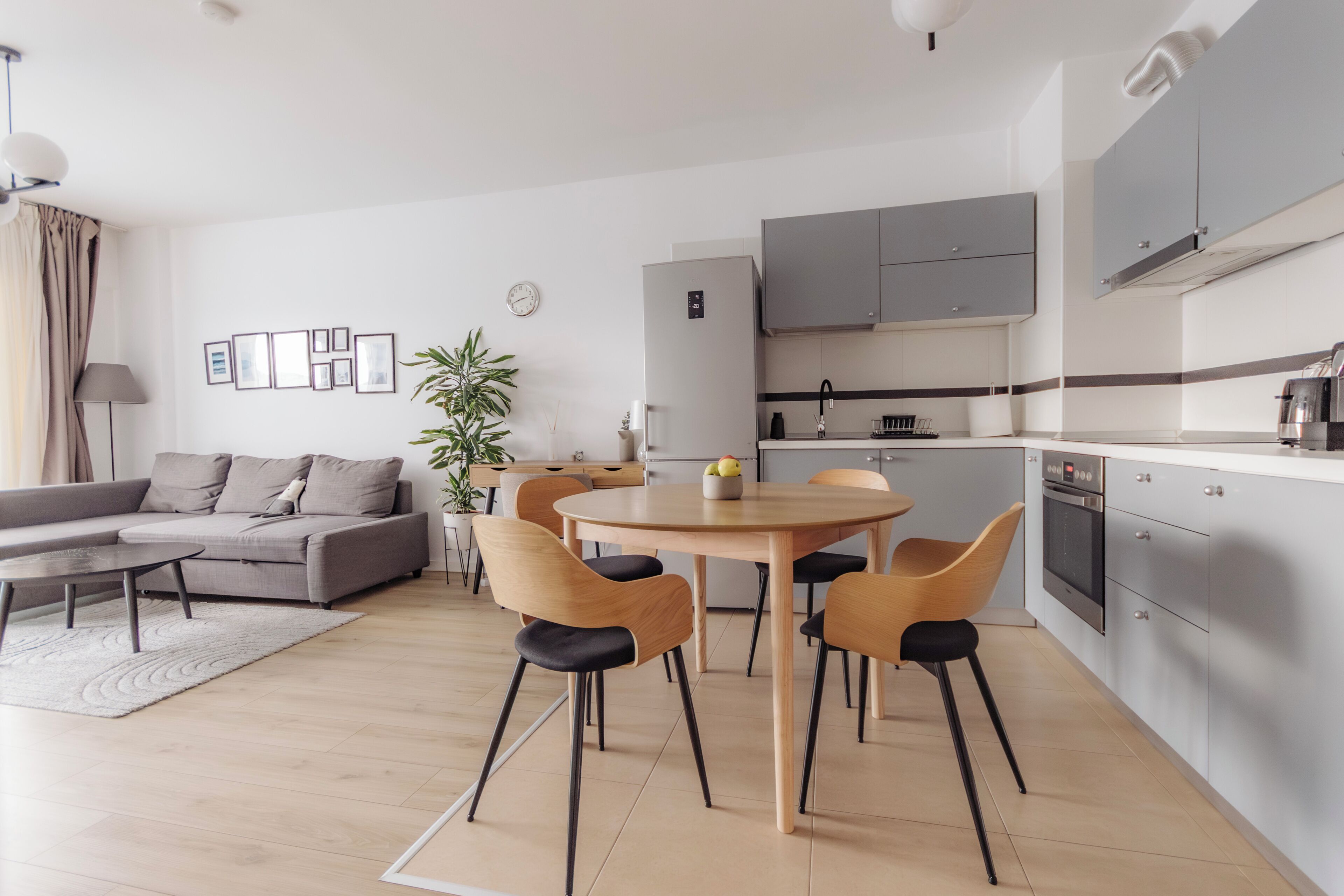 Una sala moderna con sofá, mesa de centro y mesa de comedor con sillas. Se observa una zona de cocina con armarios y electrodomésticos.