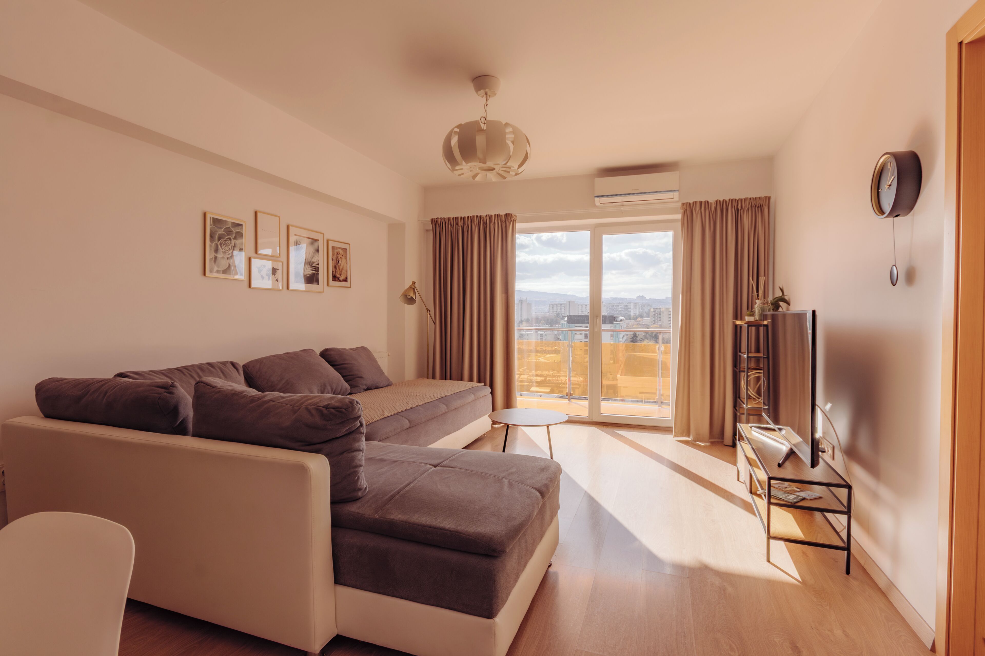 A modern living room with a sofa, a TV, and a balcony with curtains.