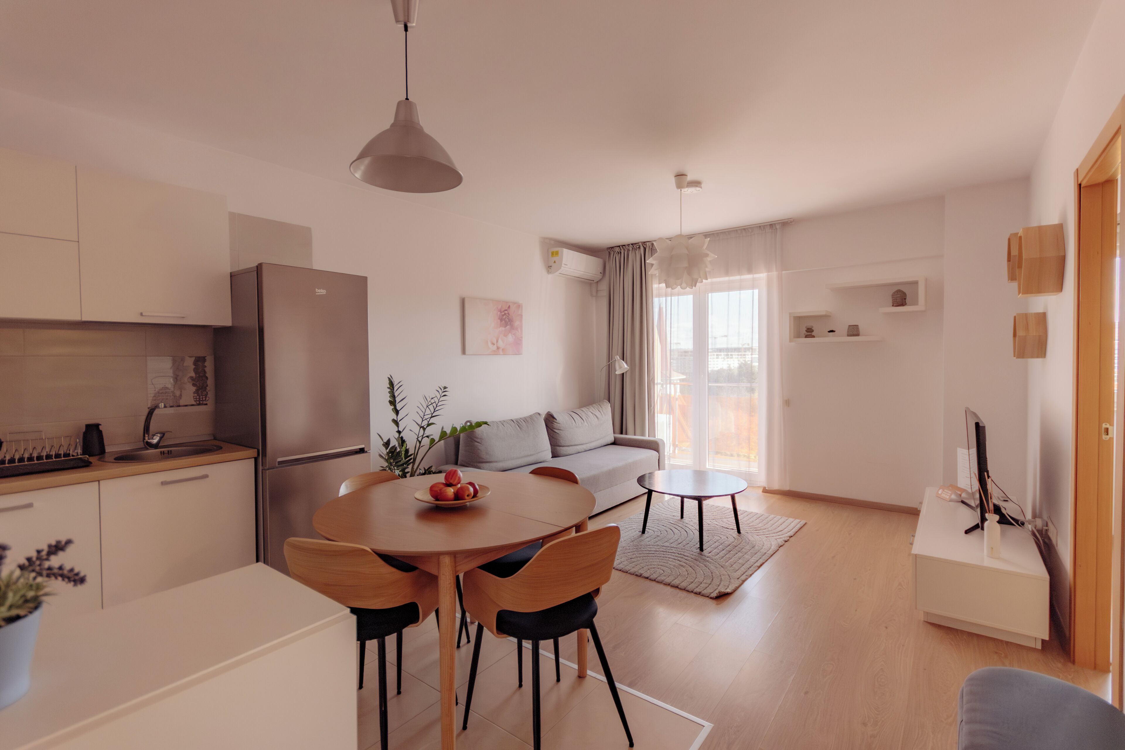 Una cocina moderna con refrigerador, mesa de comedor y sillas. Hay un sofá y una pequeña mesa en la sala de estar.