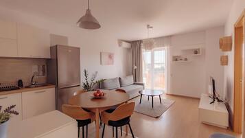 Una cocina moderna con refrigerador, mesa de comedor y sillas. Hay un sofá y una pequeña mesa en la sala de estar.
