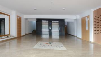 A clean, modern hallway with a 'Viva City Residence Block 2' sign, elevators, and a wooden locker area.