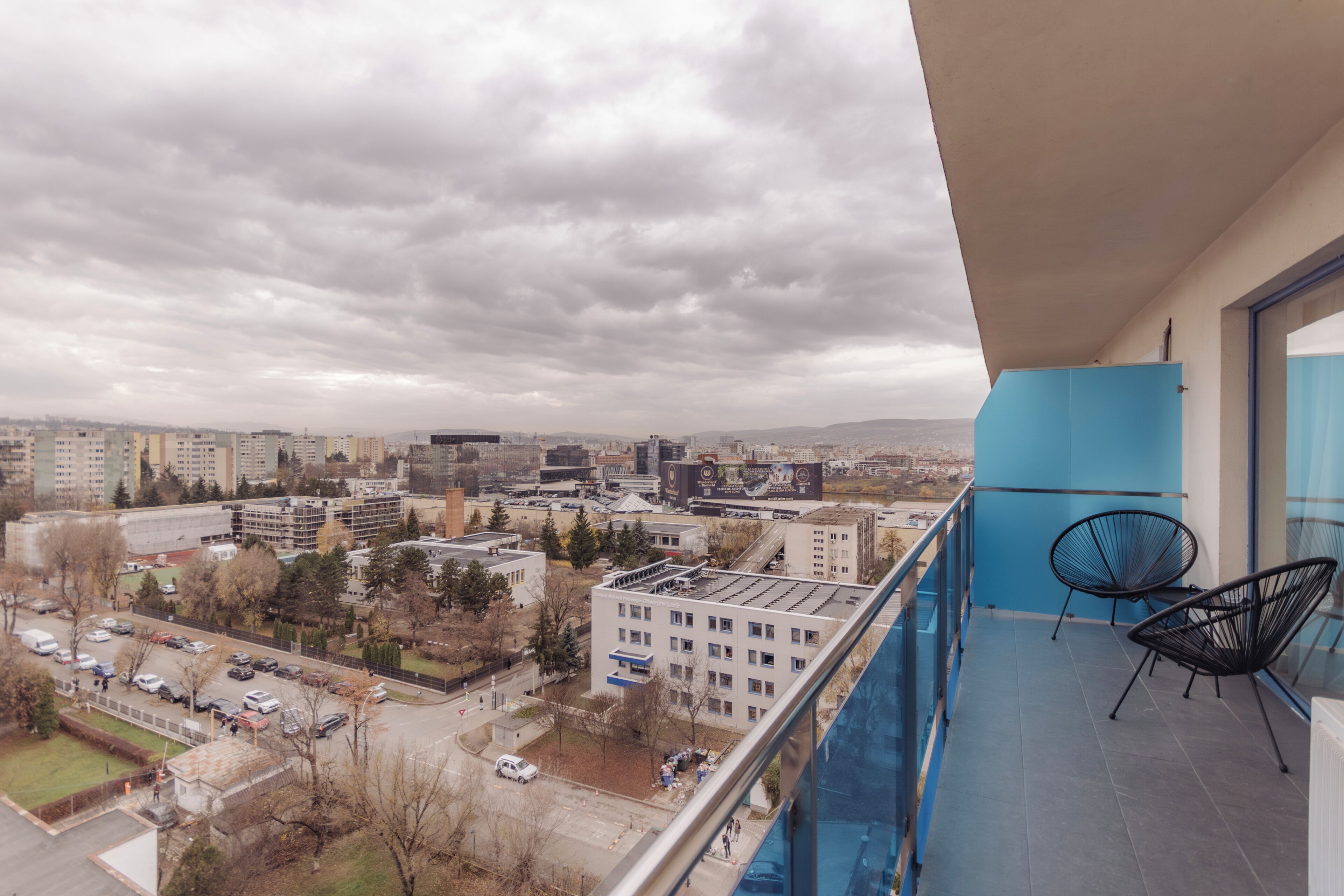 Ένα μπαλκόνι με θέα στην πόλη, δύο καρέκλες και ένας μπλε τοίχος.