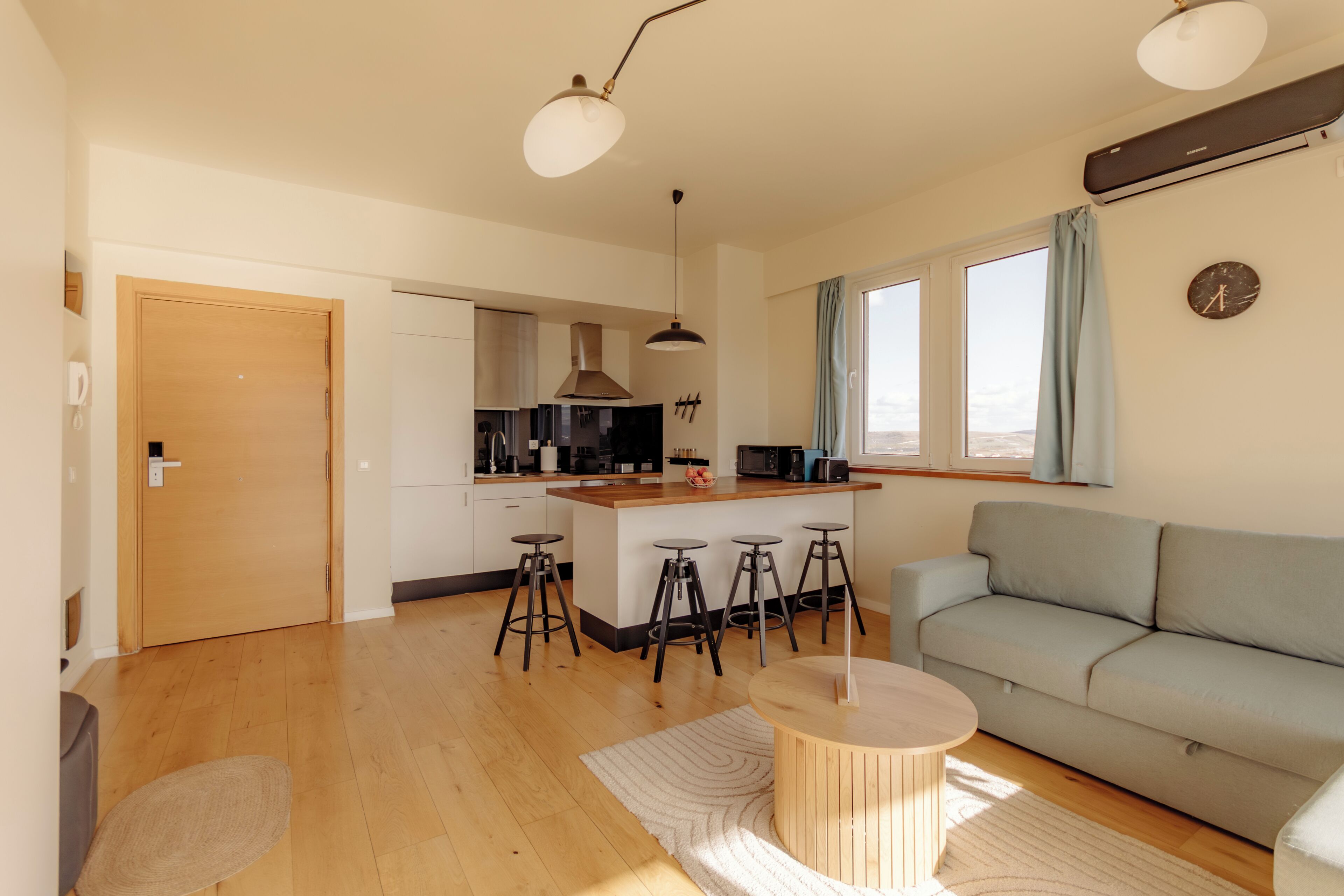 Une cuisine moderne avec un îlot central, des tabourets de bar, un canapé et une table ronde en bois.