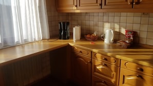 A kitchen with wooden cabinets, a coffee maker, a kettle, and a basket of bread on the counter.