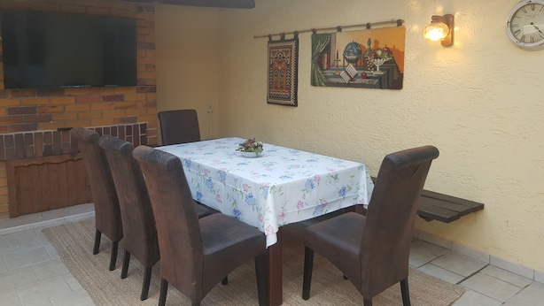 A dining area with a table set for four, surrounded by chairs, a brick fireplace, and a wall-mounted clock.