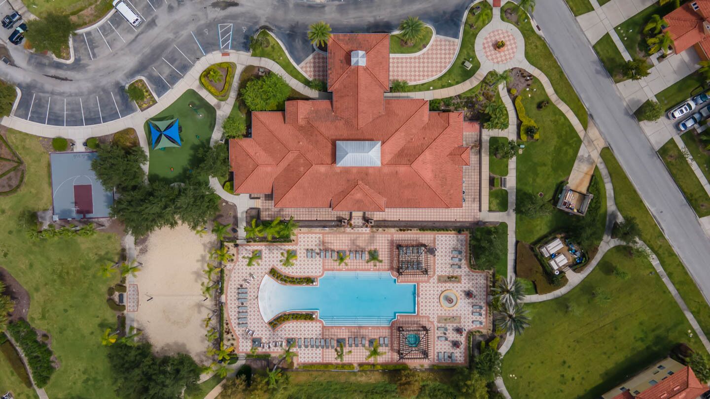 An aerial view of a hotel with a central swimming pool, a landscaped garden, and a parking area.