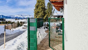 A snow-covered outdoor area with a green gate, a wooden building, and a view of snow-capped mountains in the background. - Ferienhaus mit Pool st Koloman (St. Koloman)