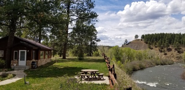 Eine rustikale Holzhütte mit Steinunterbau, einer Holzdiele und einem Picknicktisch.