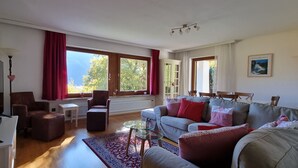 A living room with a TV, seating, a coffee table, and large windows with curtains. - Spacious, privacy and beautiful unobstructed view of the mountains and valley (Stuhlfelden)