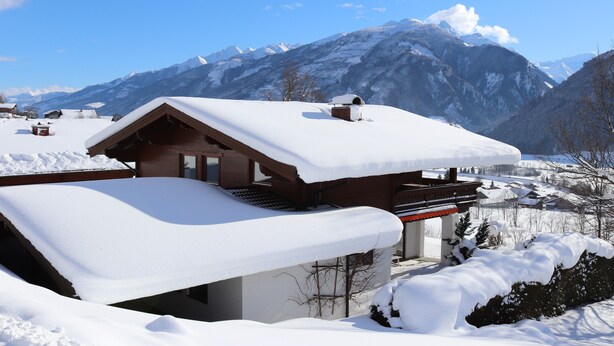 A wooden chalet with a sloped roof covered in snow, set against a backdrop of snow-covered mountains and a clear blue sky. - Spacious, privacy and beautiful unobstructed view of the mountains and valley (Stuhlfelden)