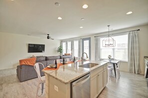 A modern kitchen with a central island, a dining area with a table and chairs, a sofa, and a large window with curtains.