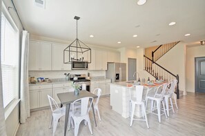 A modern kitchen with white cabinetry, a central island, and a dining area with white chairs.