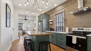 Une cuisine moderne dotée d’un îlot central, de tabourets de bar, d’un réfrigérateur en acier inoxydable, d’une cuisinière et d’un lambris en bois.