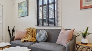 Un salon avec un canapé gris, deux tables en marbre blanc, une plante en pot et un tableau accroché au mur.
