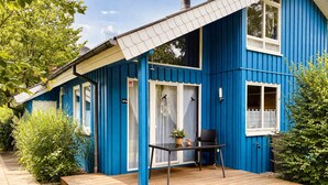 A blue house with a wooden deck, a table with chairs, and a window with a dreamcatcher.