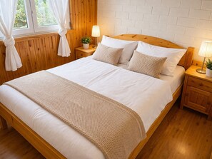 A wooden bed with white bedding, a bedside table with a lamp, and a window with curtains.