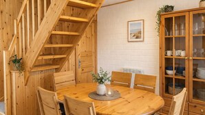 A wooden dining area with a round table, chairs, a staircase, and a cabinet with glass doors.