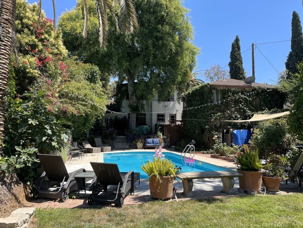 Un patio trasero con piscina, sillas de descanso y plantas en macetas.