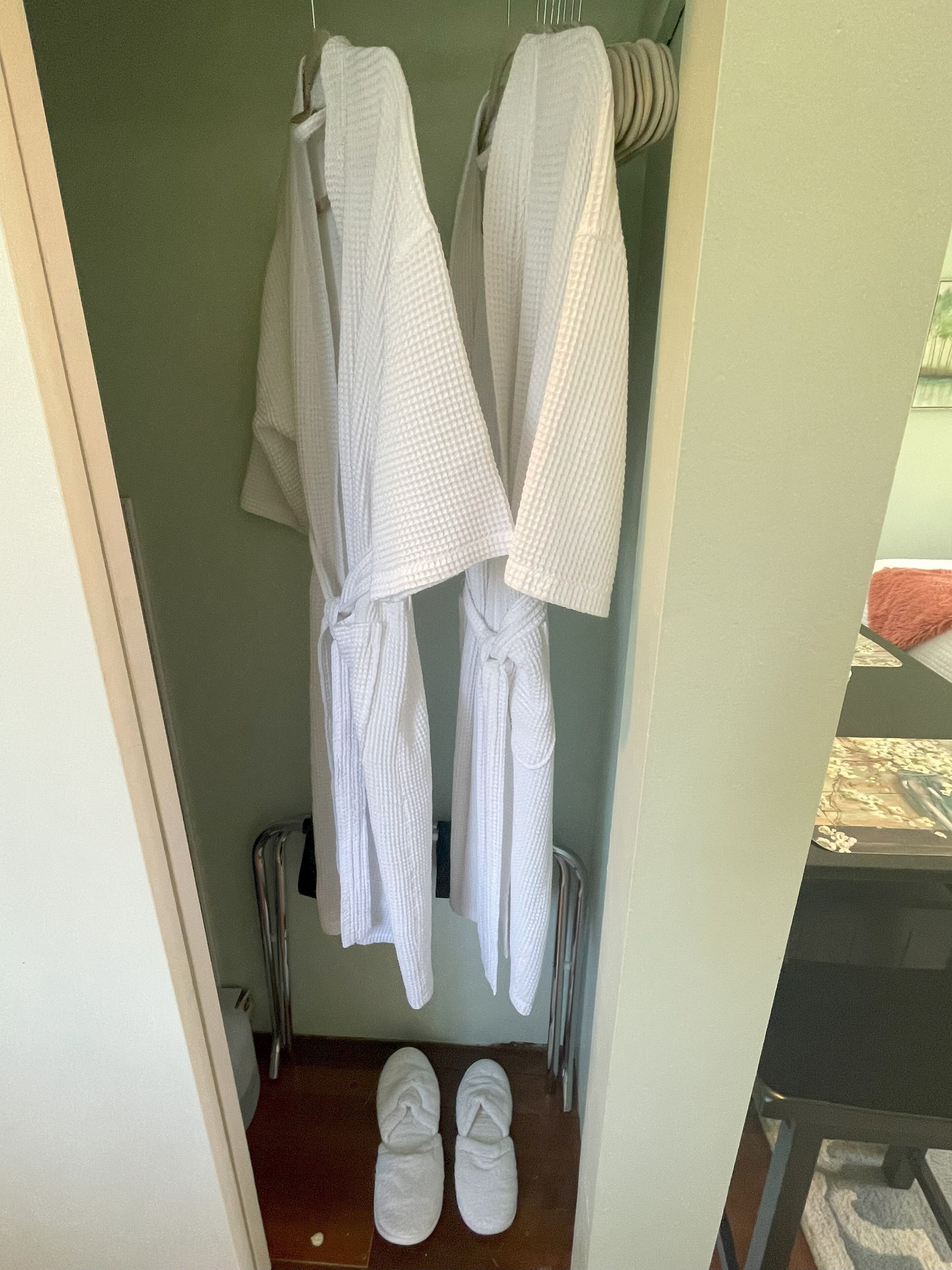 Un baño con dos toallas blancas colgadas en un perchero, un par de zapatillas blancas en el suelo y un radiador abajo.