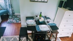 A dining area with a table set for four, including wine glasses, plates, and a bottle. There are two black chairs, a blue rug, and a white cabinet in the background.