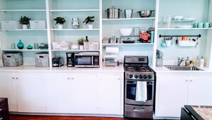 A modern kitchen with white cabinets, a stainless steel stove, a microwave, and various kitchen utensils on shelves.