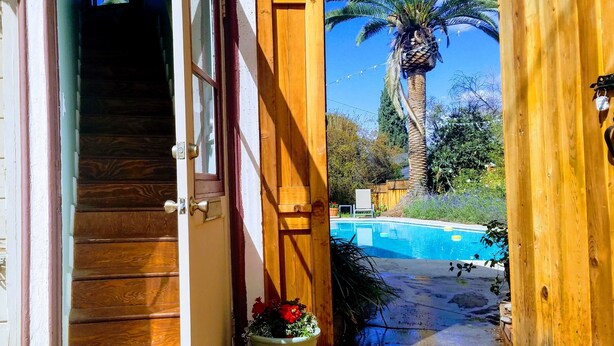 A wooden door leading to a pool area with a palm tree and a staircase.