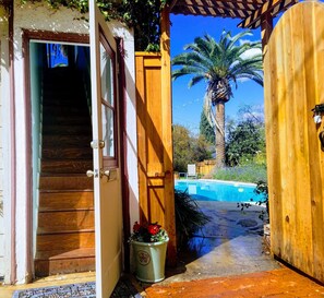 Puerta de madera que da a un área de piscina con una palmera y una escalera.