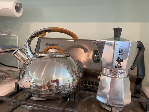 A stainless steel kettle with a wooden handle and a metal coffee press on a stove.