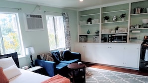 A bedroom with a bed, a blue sofa, a small table, and a kitchen area with cabinets and appliances.