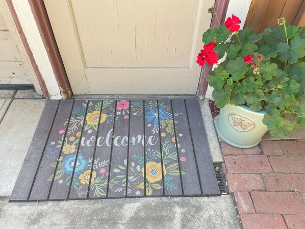 Alfombra de bienvenida con diseños florales y la palabra "welcome" frente a una puerta.