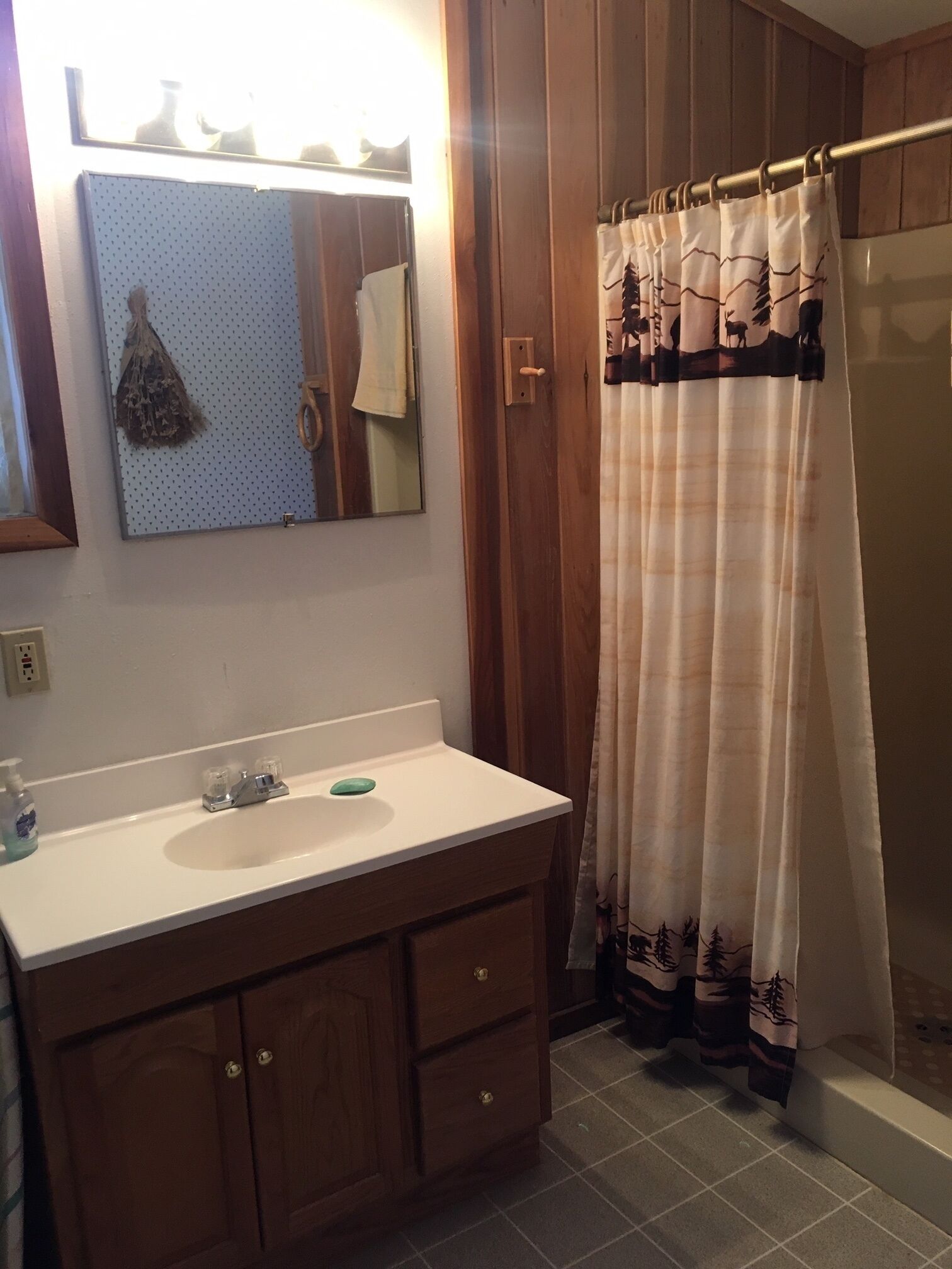 Un baño con tocador de madera, un espejo, un lavamanos y una cortina de ducha con diseño de bosque.