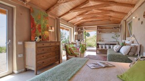 A cozy room with a wooden ceiling, a bed with a green blanket, a wooden dresser, and a dining area with a table and chairs.