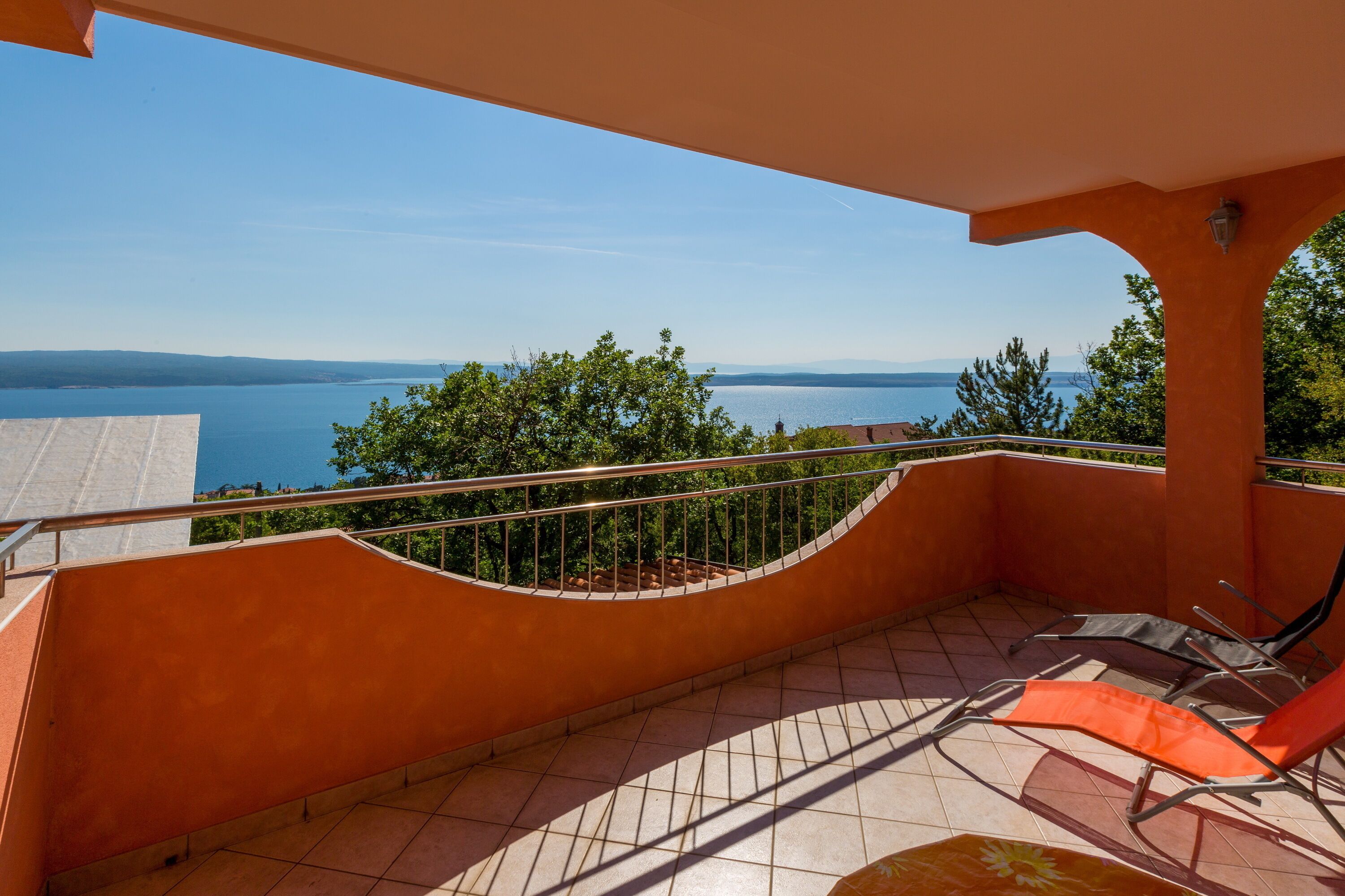 A balcony with a view of the sea, a tiled floor, and two lounge chairs.