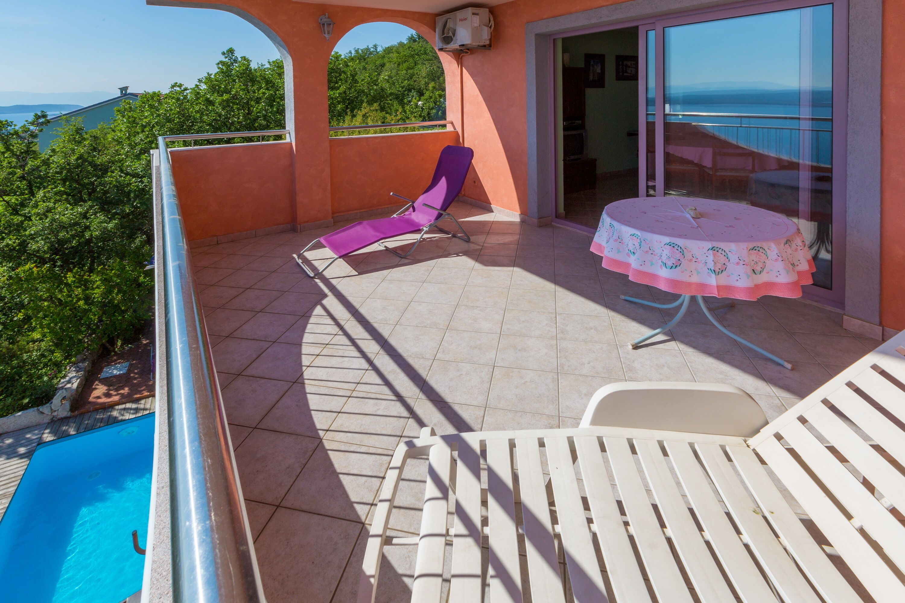 Een balkon met een zwembad, een tafel met een tafelkleed en een paarse stoel.
