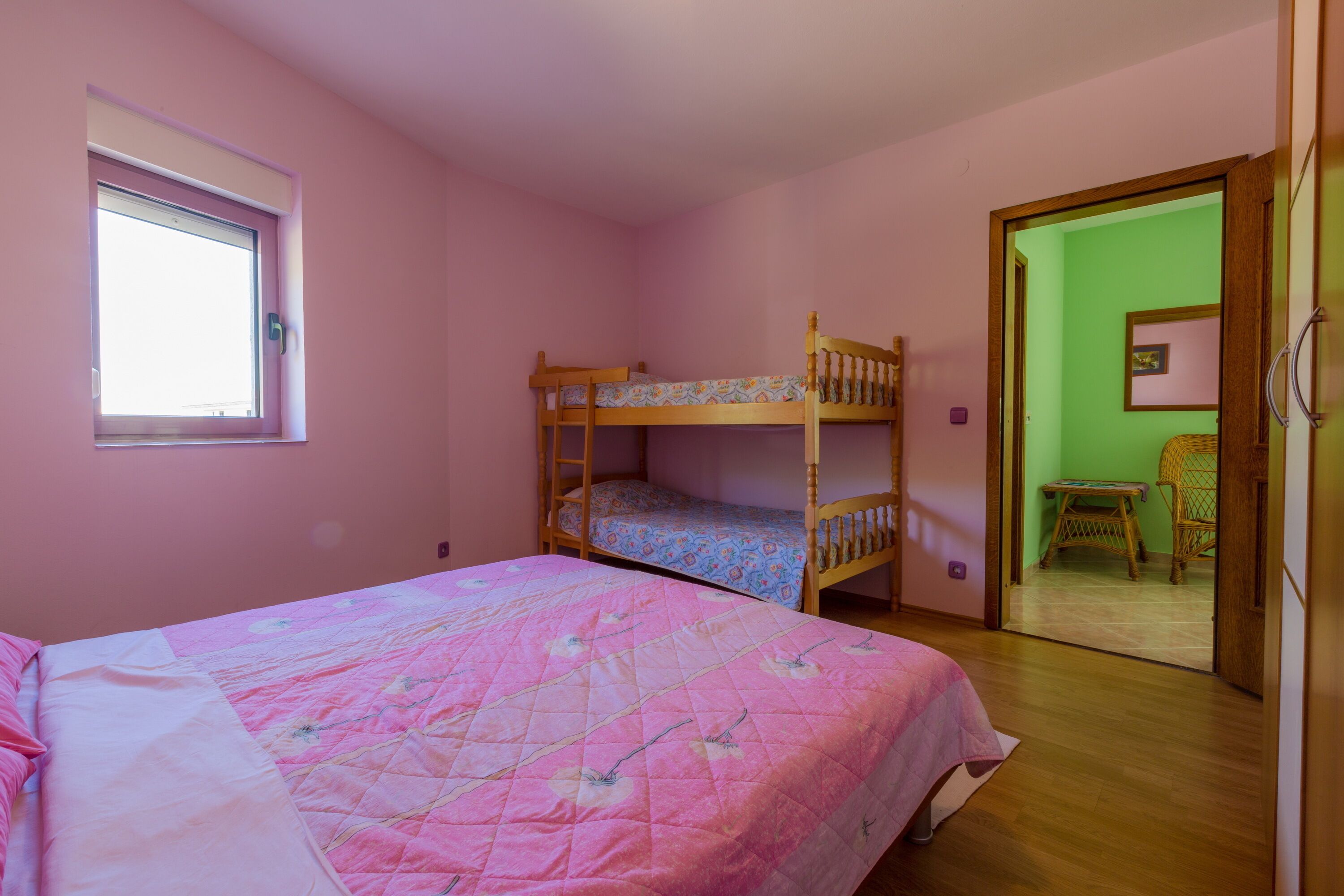 Une chambre avec un lit superposé, un lit simple, une fenêtre et une porte donnant sur une autre pièce.