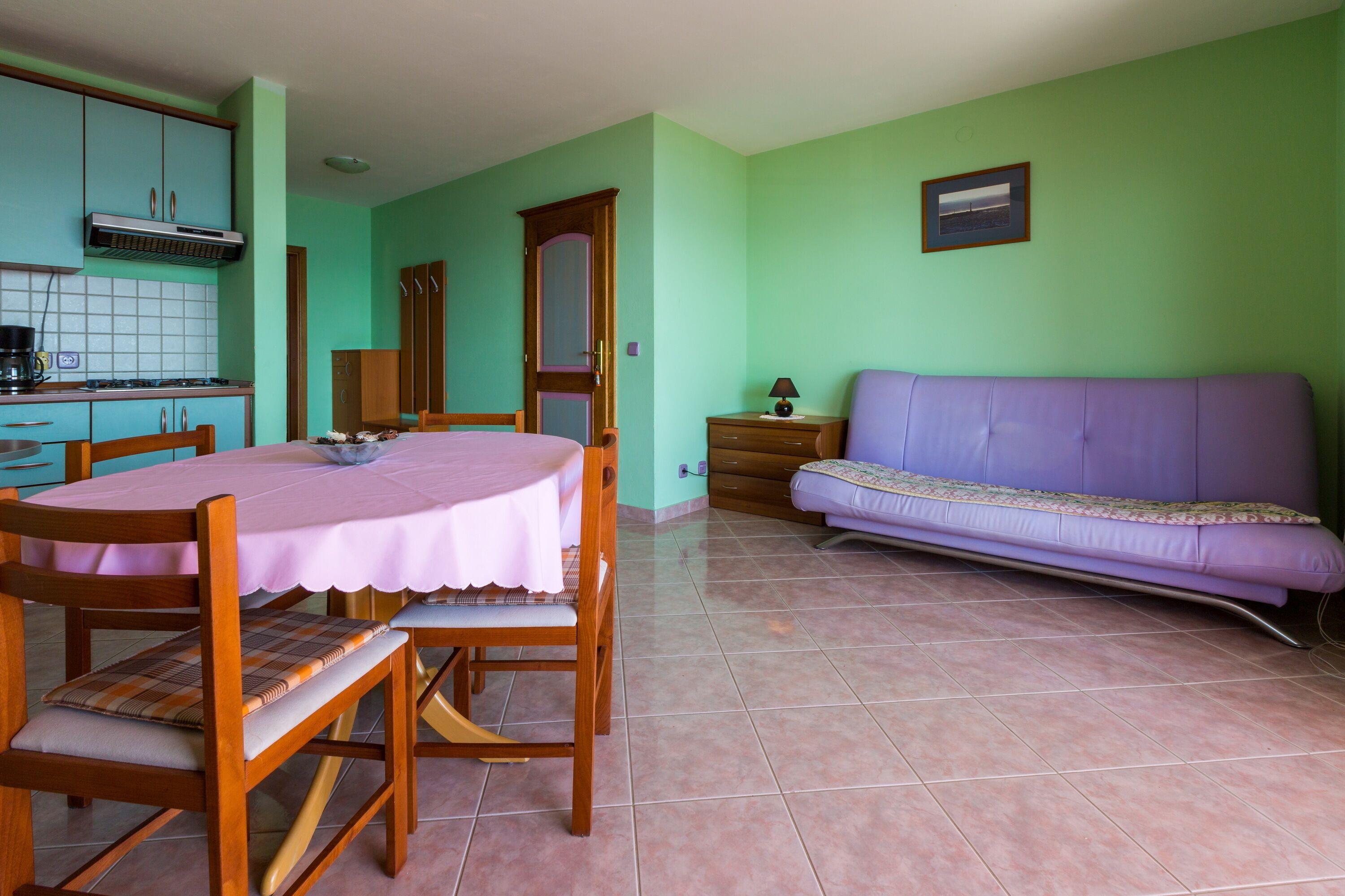 A room with a dining table, chairs, a sofa, a cabinet, and a tiled floor.
