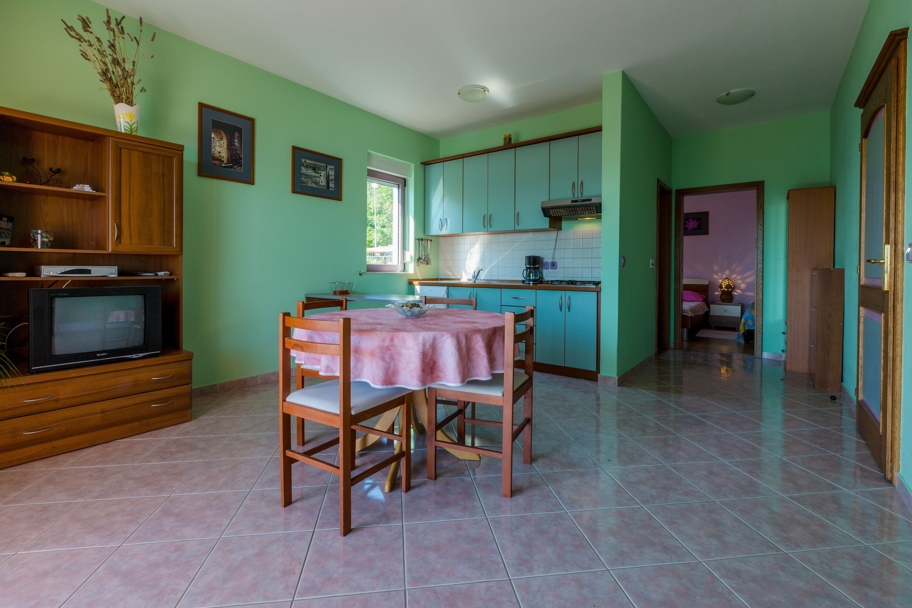A kitchen with teal cabinets, a dining table with chairs, and a television in the corner.