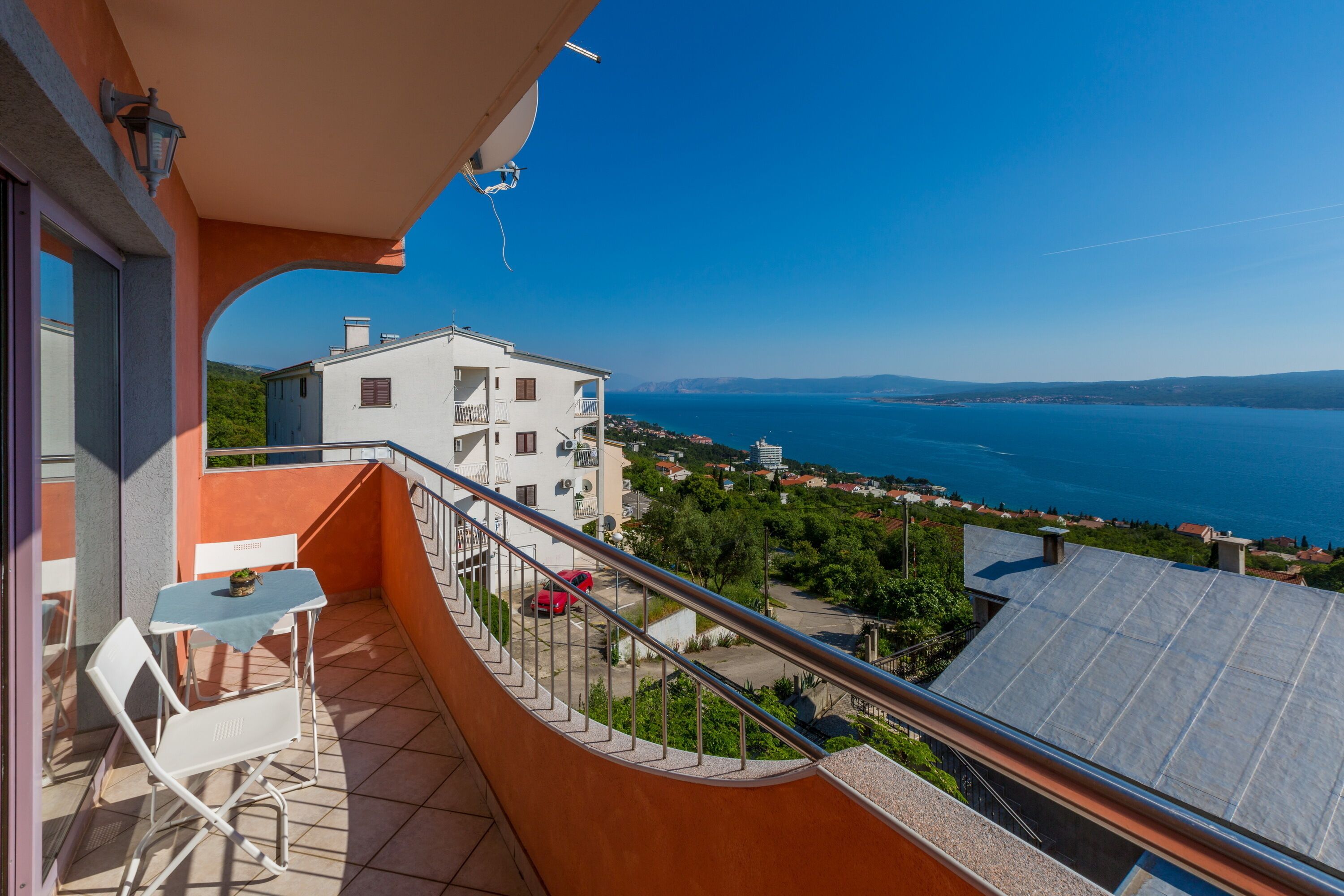 A balcony with a view of the sea and a white building in the background.