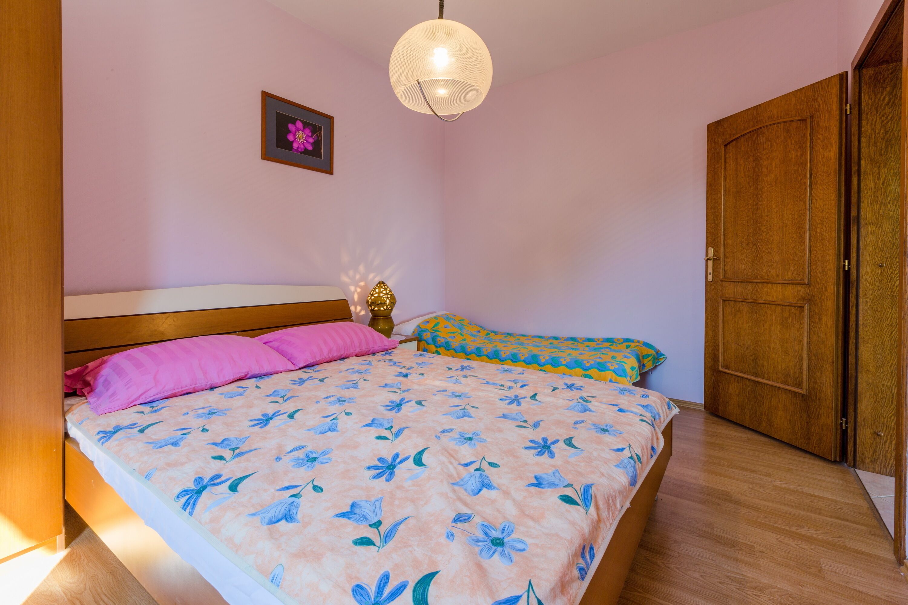 A bedroom with a bed, a bedside table, a lamp, and a wooden wardrobe.