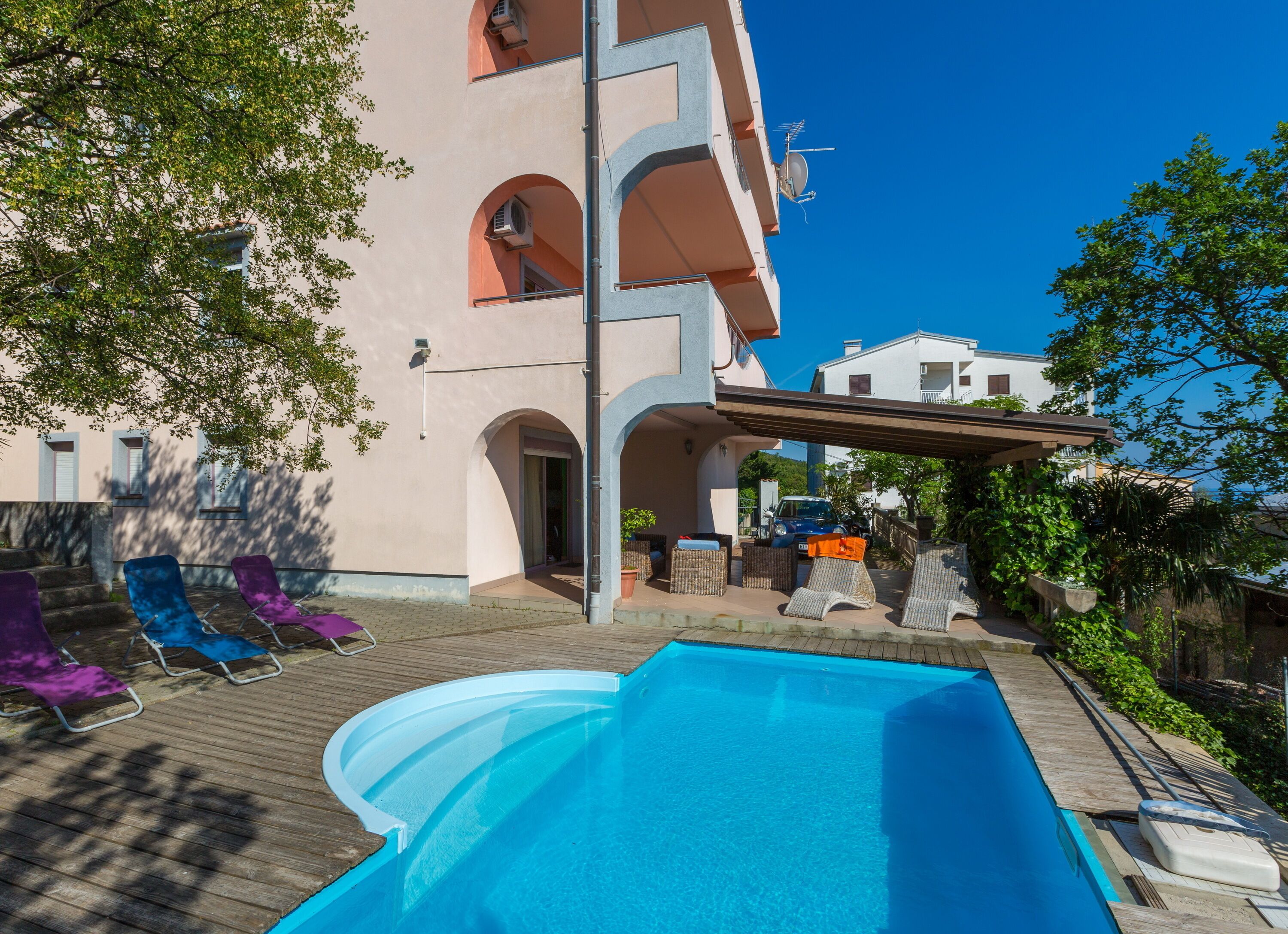 Un espace piscine avec des chaises longues, un coin salon abrité et un bâtiment doté de nombreux balcons et fenêtres.