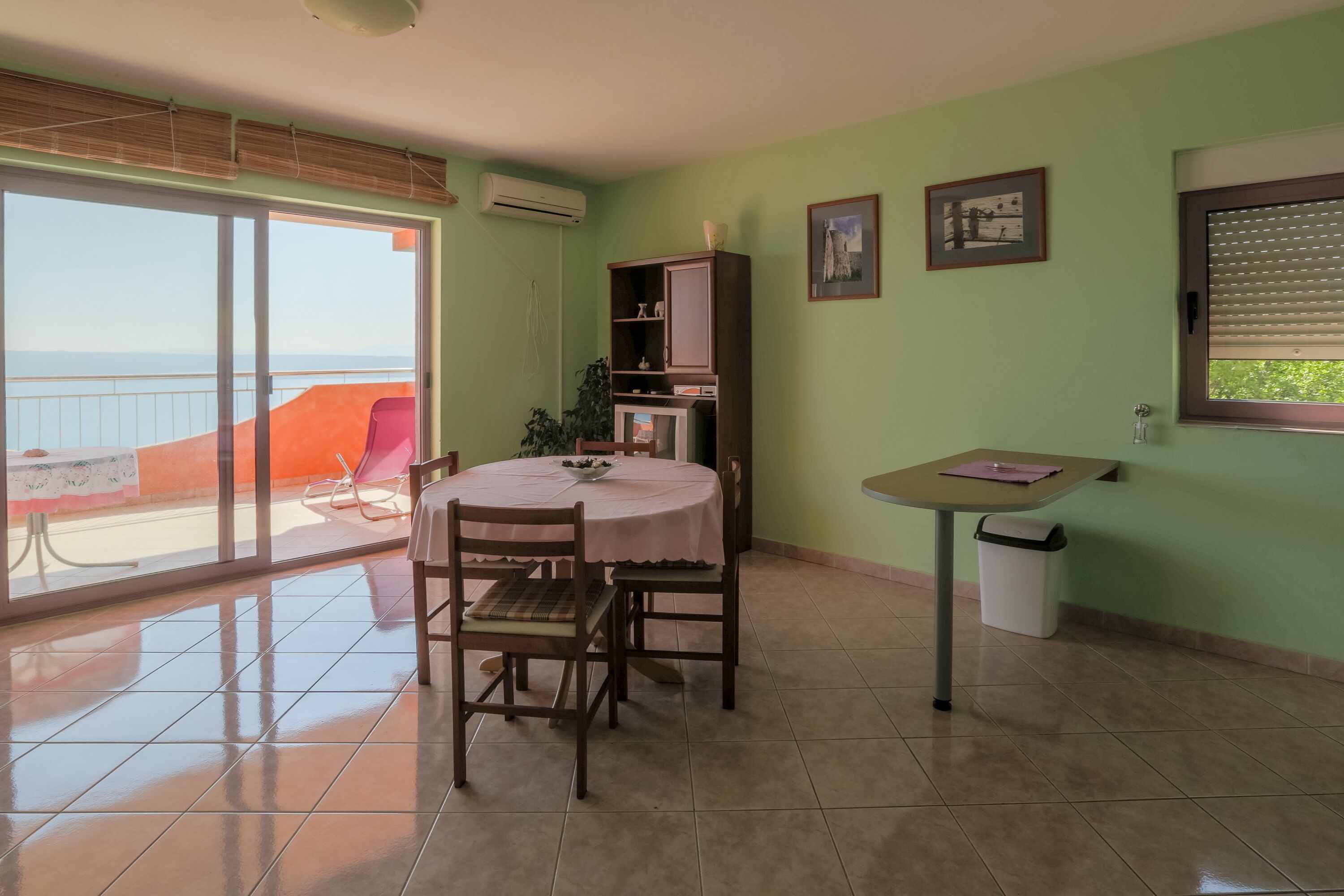 Un comedor con una mesa, sillas, un mueble bajo y una ventana con persianas.