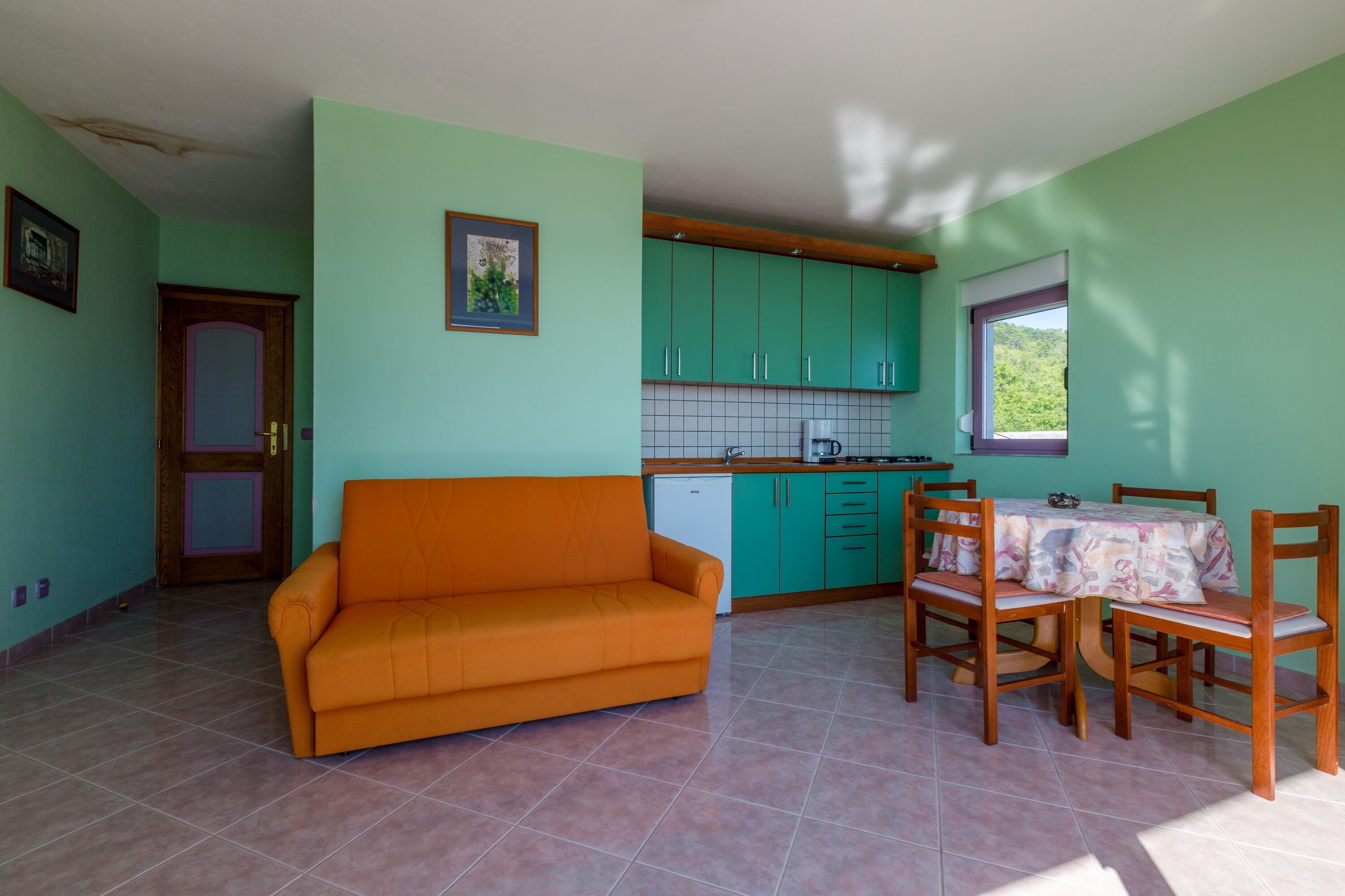 Un espacio habitable compacto con sofá, mesa de comedor, sillas, kitchenette y una puerta.