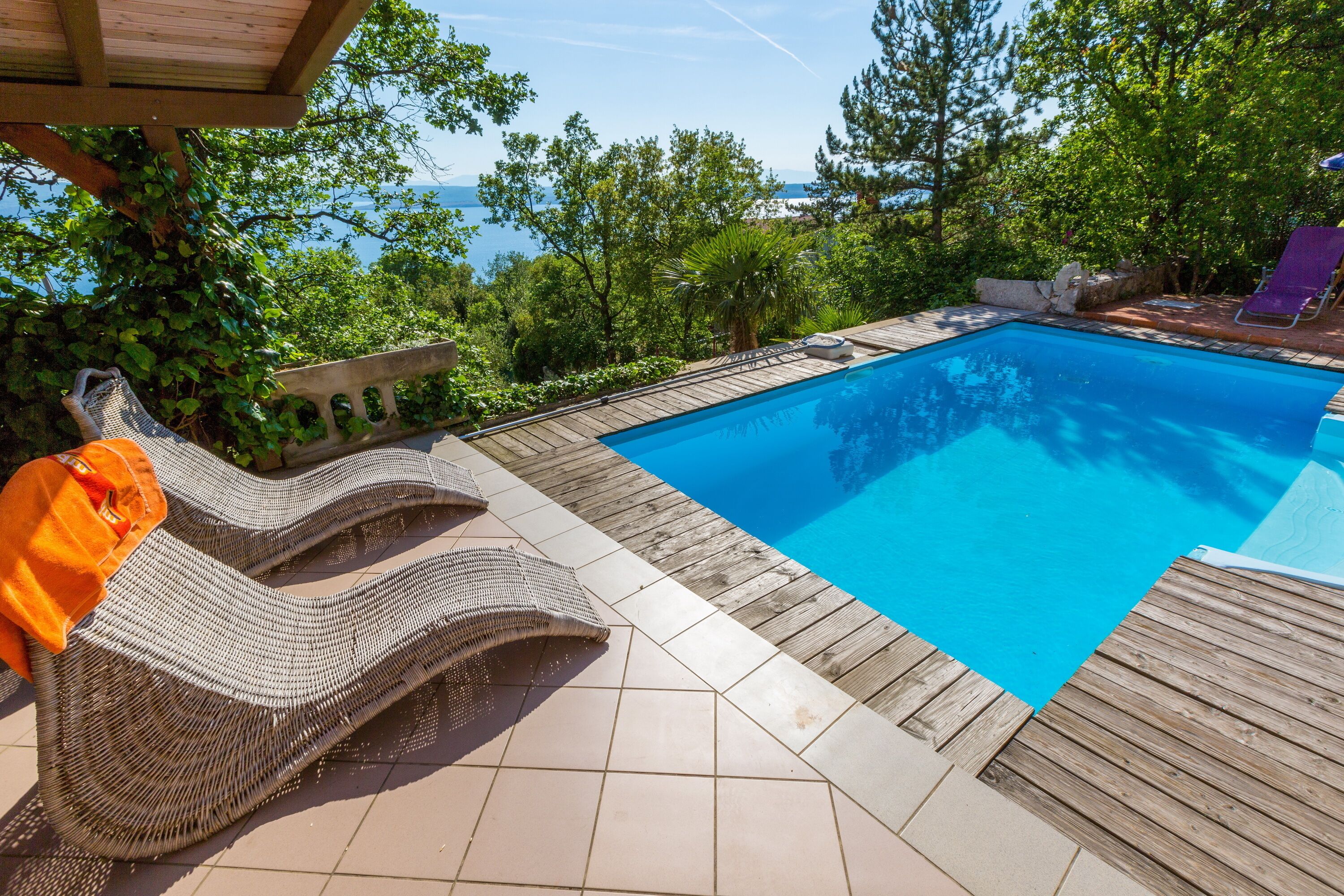 A swimming pool with wooden decking and wicker lounge chairs.