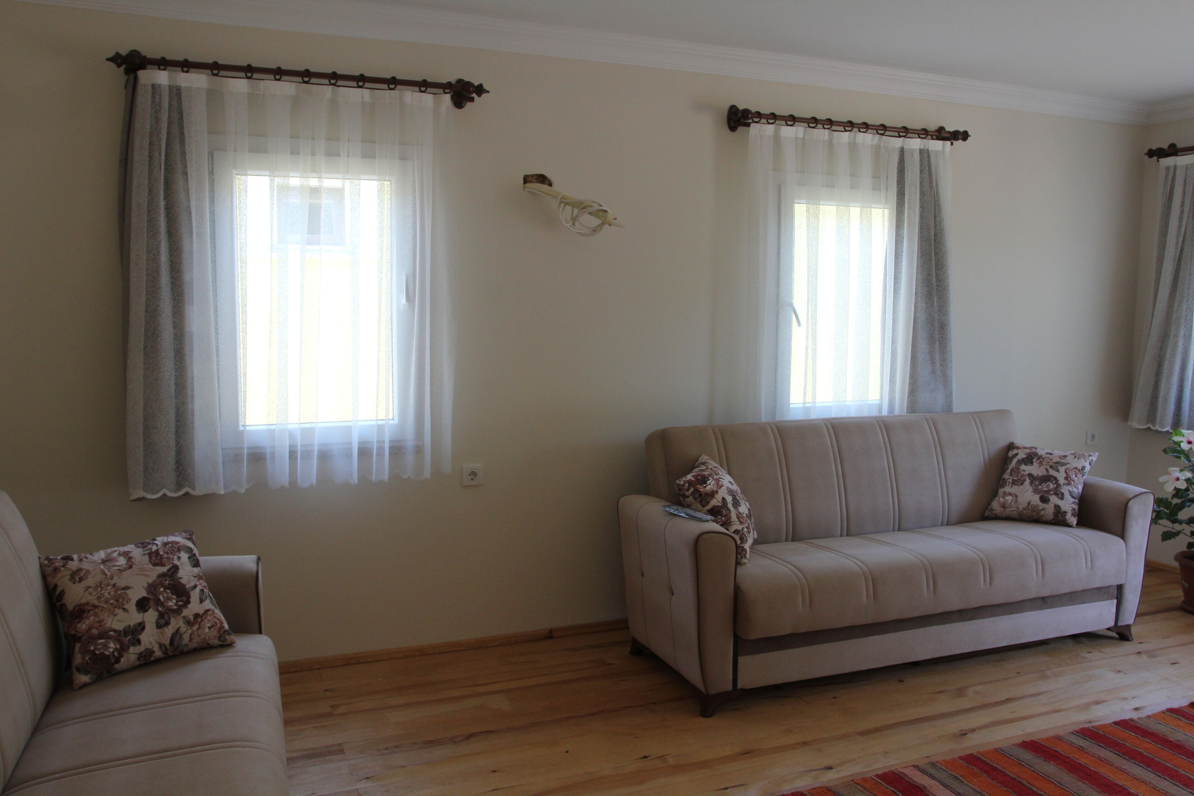 Una sala de estar con dos sofás, piso de madera y una ventana con cortinas.